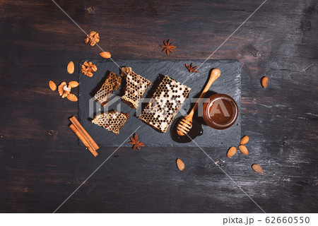 Honeycomb, bee pollen granules, honey jar with wooden dipper, almond nuts on black slate tray over dark background. Copy space. Top view. Autumn harvest concept Honeycomb, bee pollen granules, honey jar with wooden dipper, almond nuts on black slate tray over dark background. Copy space. Top view. Autumn harvest concept 62660550