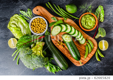 Flat lay assorted green toned vegetables on dark board, fresh organic raw food concept top view 62665820