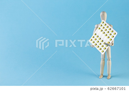 Wooden toy figure with pills on blue background. Wooden toy figure with pills on blue background. 62667101