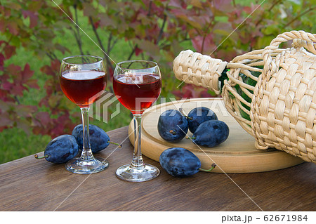 Plum alcoholic drink in two glass glasses and bottle with ripe plums in a wooden plate on a natural background 62671984