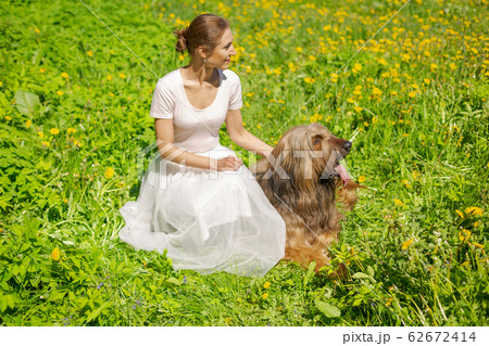 A girl in a white dress and her pet shepherd dog, briard are playing on the spring meadow. A girl in a white dress and her pet shepherd dog, briard are playing on the spring meadow. 62672414
