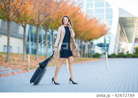 Smiling female passenger proceeding to exit gate pulling suitcase through airport concourse Smiling female passenger proceeding to exit gate pulling suitcase through airport concourse 62672789
