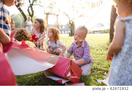 Down syndrome child with friends on birthday party outdoors, opening presents. 62672832