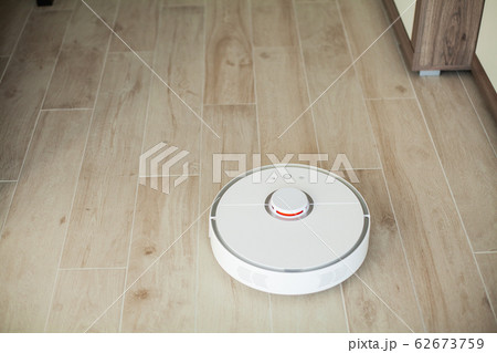 Smart House. Vacuum cleaner robot runs on wood floor in a living room Smart House. Vacuum cleaner robot runs on wood floor in a living room 62673759
