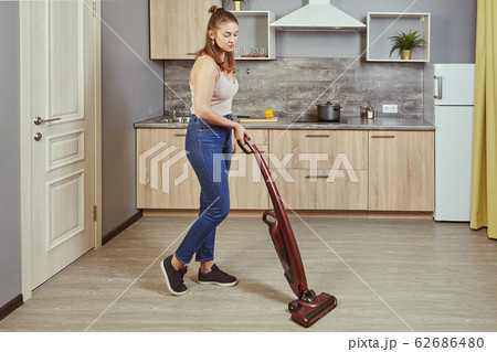 One young woman uses a wireless vacuum cleaner. One young woman uses a wireless vacuum cleaner. 62686480