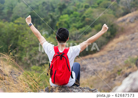 Young tourist man with backpack sitting on rocky mountain and raised hand for the winner. Young tourist man with backpack sitting on rocky mountain and raised hand for the winner. 62687573