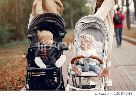 Two young mothers walking in a autumn park with carriages Two young mothers walking in a autumn park with carriages 62687648