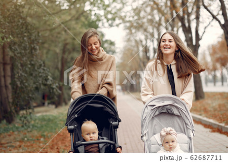 Two young mothers walking in a autumn park with carriages Two young mothers walking in a autumn park with carriages 62687711