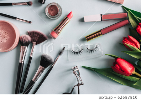 Makeup cosmetics and red peony flowers on a blue background. Brushes, shadow palette, lipstick and eyelashes for the care and beauty of a woman's face 62687810