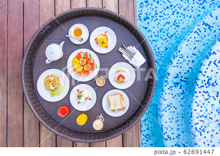 Flotaing breakfast tray around outdoor swimming pool with bread fruit egg coffee and juice Flotaing breakfast tray around outdoor swimming pool with bread fruit egg coffee and juice 62691447