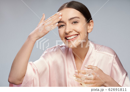 Joyful pretty girl washing face with foaming cleanser 62691811