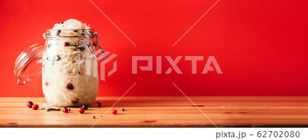 Fermented cabbage with cranberry in glass jar over wooden and red background. Probiotics food concept. Preserved vegetarian diet, homemade fermentation. Banner with copy space Fermented cabbage with cranberry in glass jar over wooden and red background. Probiotics food concept. Preserved vegetarian diet, homemade fermentation. Banner with copy space 62702080