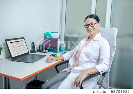 Female dark-haired doctor in eyewear smiling brightly Female dark-haired doctor in eyewear smiling brightly 62703685