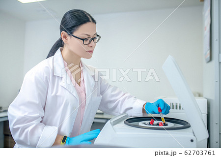 Technician in blue gloves inserting glass tubes to centrifuge 62703761