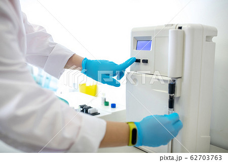 Technician in blue gloves pushing the start button on centifuge 62703763