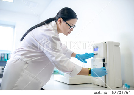 Technician in blue gloves pushing the start button on centifuge 62703764
