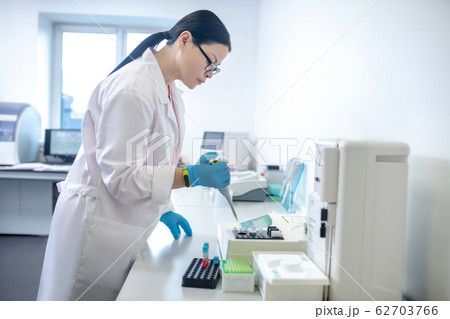 Technician in blue gloves pouring blood sample into the test tube and looking busy 62703766
