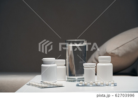 Pills and glass of water near sofa, dark 62703996