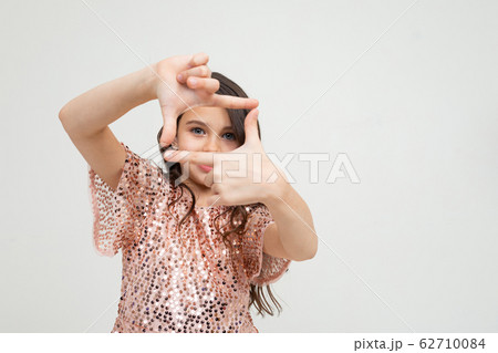 portrait of a cute smiling teenager girl in a shiny dress photographing with her fingers on a white 62710084