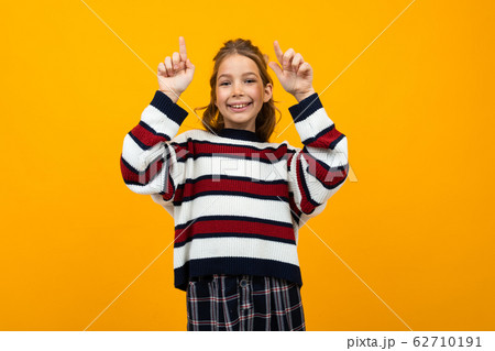cute teen girl in a striped casual sweater shows on the wall with copy space 62710191