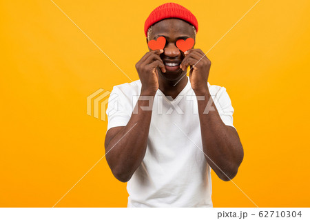 Smiling American dark-skinned man in a white T-shirt holds two small eye-shaped postcards for Smiling American dark-skinned man in a white T-shirt holds two small eye-shaped postcards for 62710304