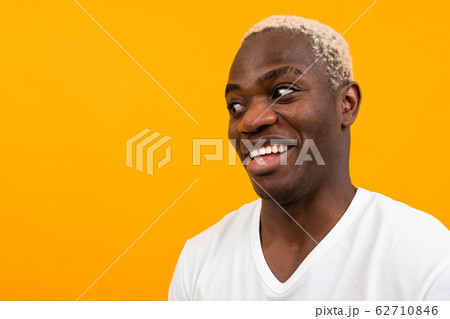 charismatic african man in a white t-shirt with a mock looks surprised to the side on a yellow charismatic african man in a white t-shirt with a mock looks surprised to the side on a yellow 62710846