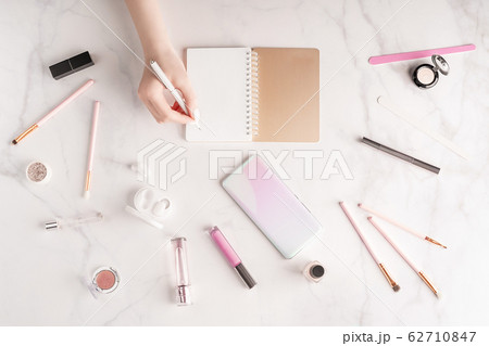 Feminine workspace in flat lay style with female hand writing in notepad, up-to-date smartphone mockup, cosmetics and manicure products on marble background. Woman's freelance concept. Feminine workspace in flat lay style with female hand writing in notepad, up-to-date smartphone mockup, cosmetics and manicure products on marble background. Woman's freelance concept. 62710847