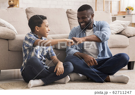 Cheerful Black Preteen Boy Fist Bumping With His Dad At Home Cheerful Black Preteen Boy Fist Bumping With His Dad At Home 62711247