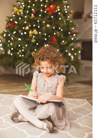 Girl writes letter to Santa near christmas tree 62712111