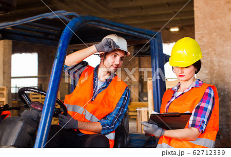 Warehouse manager checking order list. People in protective helmet, vest and gloves at factory. Warehouse manager checking order list. People in protective helmet, vest and gloves at factory. 62712339