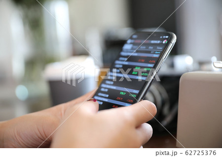 Female hand with smartphone trading stock online in coffee shop , Business concept Female hand with smartphone trading stock online in coffee shop , Business concept 62725376