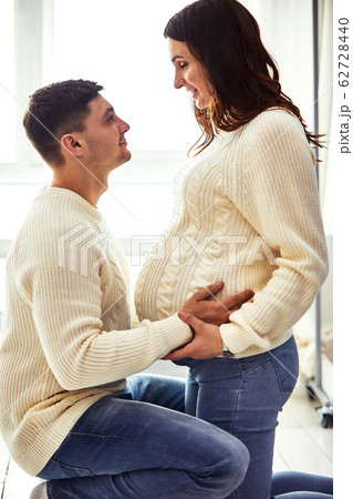 Close up portrait of expecting teenage couple laughing happily, embracing baby in belly together. Couple dressed in blue and white colors. 62728440