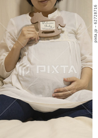 フォトフレームを持ってお腹に手を当てる妊婦さんのマタニティフォト フォトフレームを持ってお腹に手を当てる妊婦さんのマタニティフォト 62728716