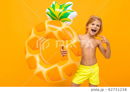 Handsome boy in swimming trunks holds a rubber ring, smiles and gesticulates isolated on orange Handsome boy in swimming trunks holds a rubber ring, smiles and gesticulates isolated on orange 62731238