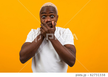 handsome surprised american guy in a white t-shirt closes his mouth with his hands from surprise on 62731338