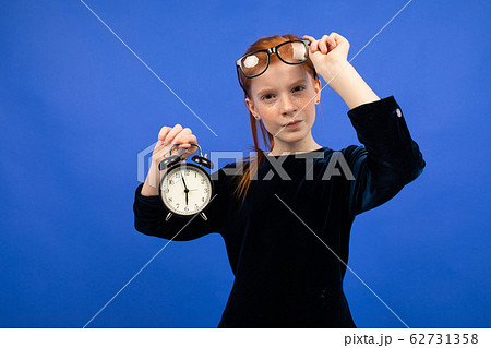 serious red-haired teenager girl in glasses in a black dress recalls punctuality holding an alarm serious red-haired teenager girl in glasses in a black dress recalls punctuality holding an alarm 62731358