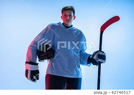 Young male hockey player with the stick on ice court and white background in neon light Young male hockey player with the stick on ice court and white background in neon light 62740517