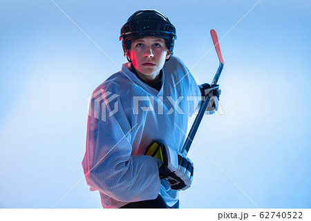 Young male hockey player with the stick on ice court and white background in neon light Young male hockey player with the stick on ice court and white background in neon light 62740522