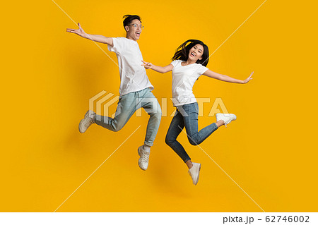 Emotional asian couple jumping over yellow background 62746002