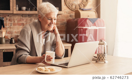 Happy Aged Lady Relaxing In Kitchen With Laptop And Coffee Happy Aged Lady Relaxing In Kitchen With Laptop And Coffee 62746273