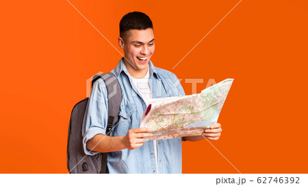 Happy traveler looking at city map over orange background Happy traveler looking at city map over orange background 62746392