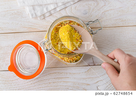 Woman hand taking universal seasoning with wooden spoon from clip top glass jar on a kitchen table. 62748654