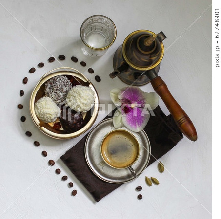 espresso in a brass cup with a turkish coffee pot, sweets, an orchid flower and a half-heart-shaped coffee bean pattern 62748901