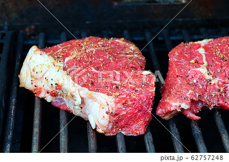Raw seasoned steaks on a BBQ grill 62757248