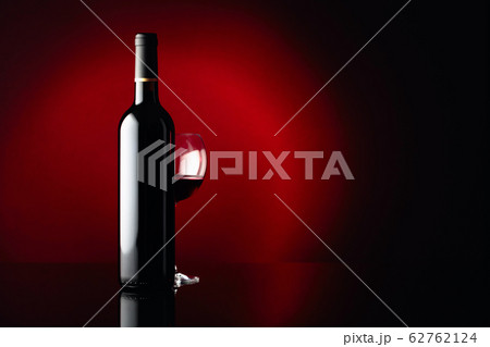 Glass and bottle of red wine on a black reflective Glass and bottle of red wine on a black reflective 62762124