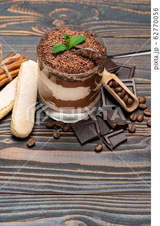 Classic tiramisu dessert in a glass cup, pieces of chocolate and savoiardi cookies on wooden background 62770056
