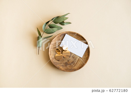 Natural branch with leaves and gold earrings in wooden plate on beige background 62772180