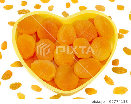 Heart shaped bowl of dried apricots isolated on white background with raisins 62774158