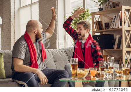 Excited, happy friends watch sport match together on the couch at home Excited, happy friends watch sport match together on the couch at home 62775046