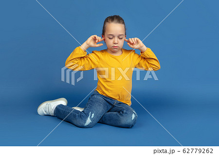 Portrait of sad little girl sitting on blue studio background, autism concept Portrait of sad little girl sitting on blue studio background, autism concept 62779262